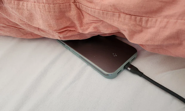 Smartphone bedraad aan de oplader onder een kussen Smartphone bedraad aan de oplader onder een kussen