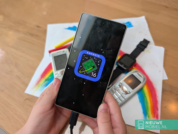 Kinderhand houdt Android-smartphone vast Kinderhand houdt Android-smartphone vast met op de achtergrond diverse dumbphones op een tafel met een kleurrijke tekening van een regenboog